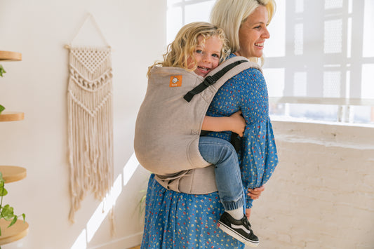 A child sitting in a back carry on their mother's back.