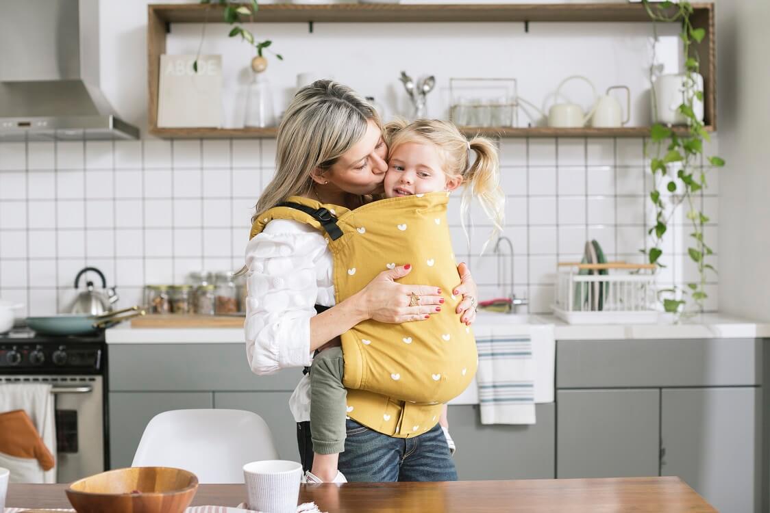 Caregiver cuddling a preschooler and wearing her in an inward facing front carry in an ergomic preschool carrier by Baby Tula.