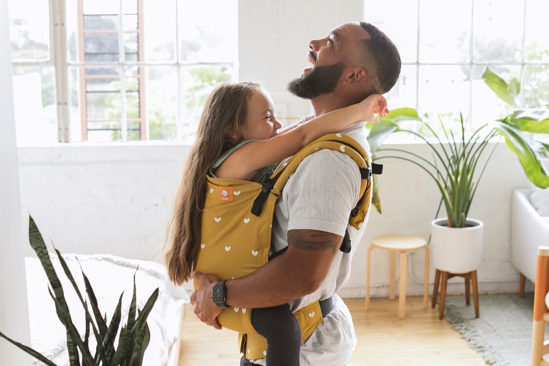 Dad goofing around with a preschooler wearing her in an inward facing front carry in an ergomic preschool carrier by Baby Tula.