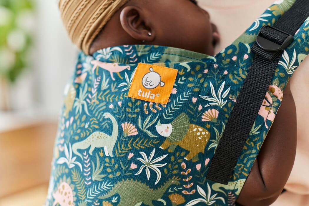 A closeup on a baby carried in Tula Free-to-Grow carrier with fun, lush print featuring our prehistoric dino friends