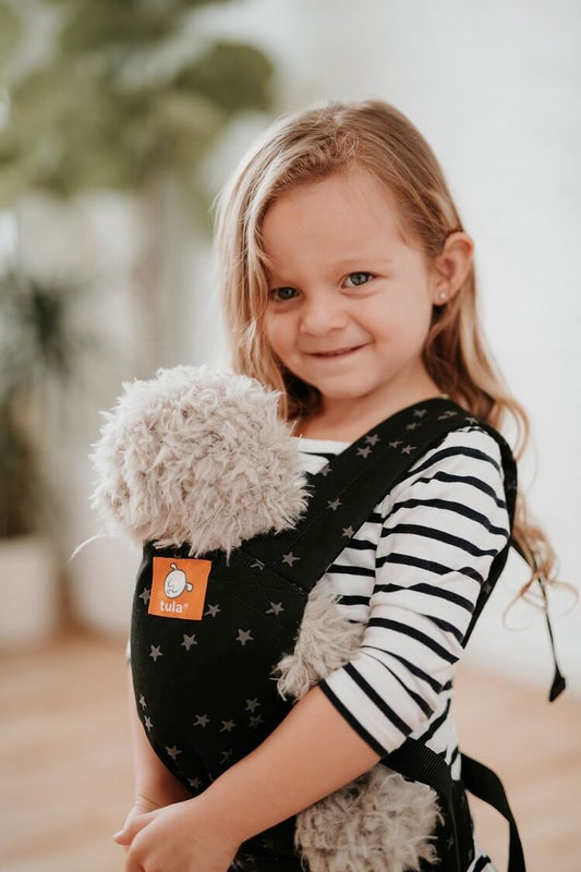 A little girl is carrying the Tula Mini Toy and Doll Carrier Discover.