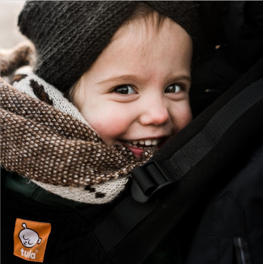 A closeup of a smiling child in a baby carrier from Tula.