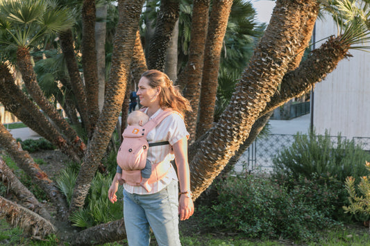 A mother and her baby using a Tula Baby Carrier in front of a palm tree