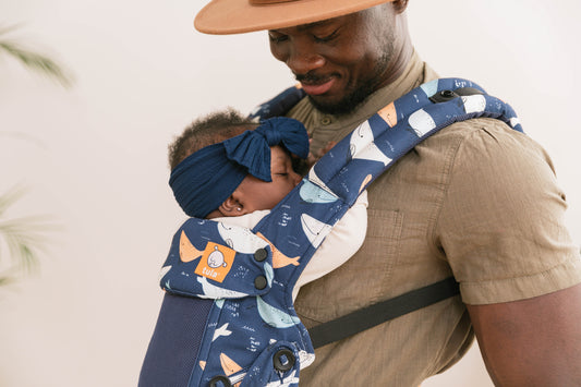 A father looking down at his child in an Explore Baby Carrier.