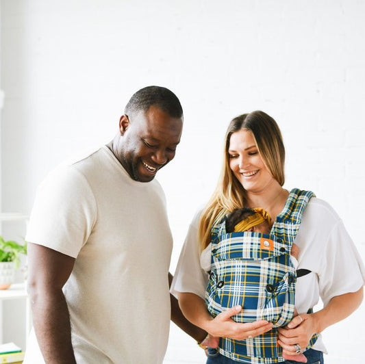 Happy mother and father gathered around their baby that is sleeping in a baby carrier from Tula.