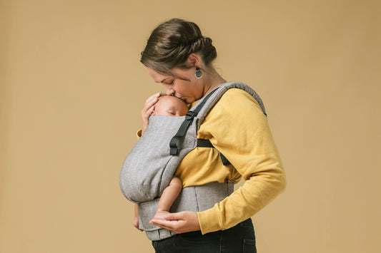 A mother giving her child a kiss on the forehead, while babywearing.