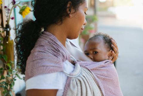 A mother breastfeeding her child while using a Tula Ring Sling.