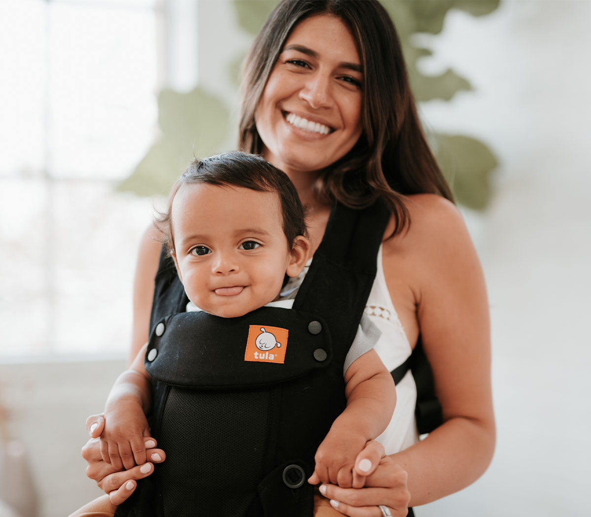 A mother and her child looking into the camera while using a Tula Explore Baby Carrier.