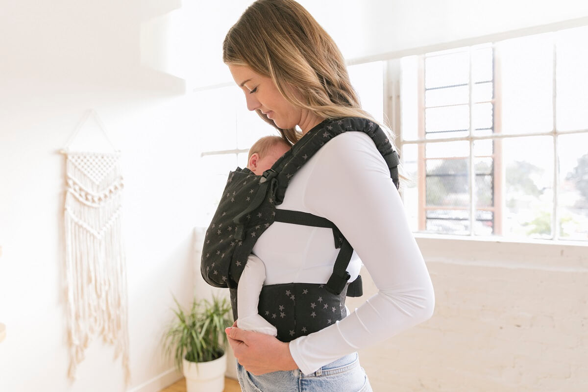 A mother carrying her baby in the ergonomic Free-to-Grow Baby Carrier Discover from Tula.