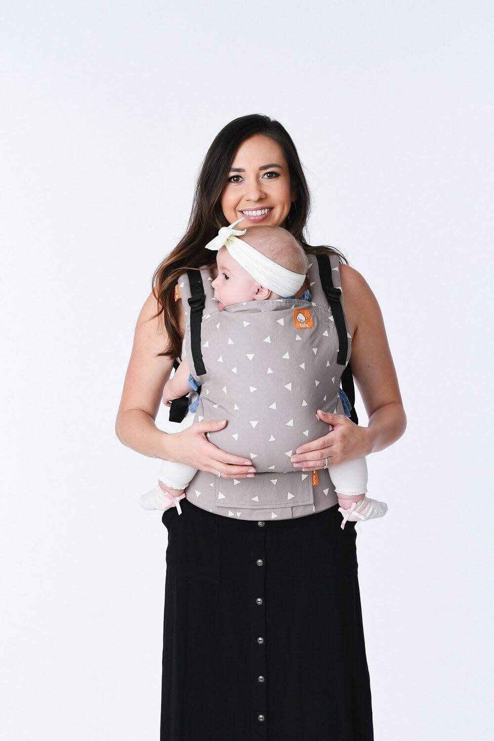 A mother smiling into the camera while using the ergonomic Free-to-Grow Baby Carrier Sleepy Dust from Tula.