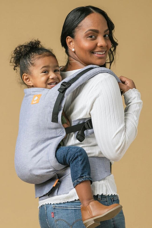 Toddler being worn in a back carry position in a hip healthy baby carrier finished in a herringbone weave