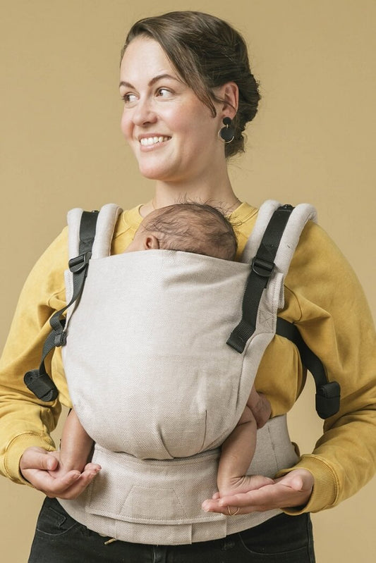A mother carrying her baby in the ergonomic Free-to-Grow Carrier Linen Sand from Tula.