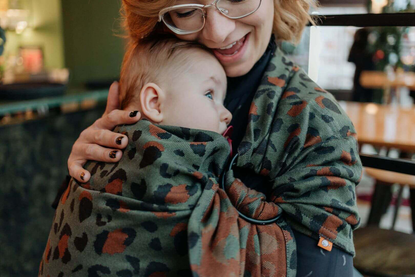 Closeoup of caregiver with infant in a ring sling baby carrier with a green leopard print.