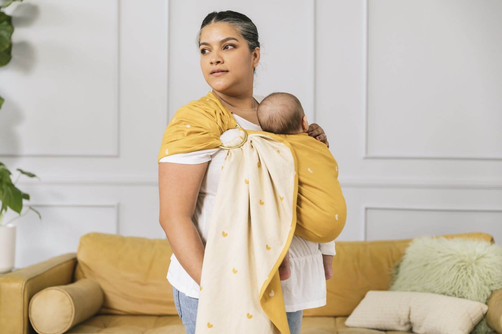 Small infant being worn in a baby sling from birth with a heart design in mustard yellow