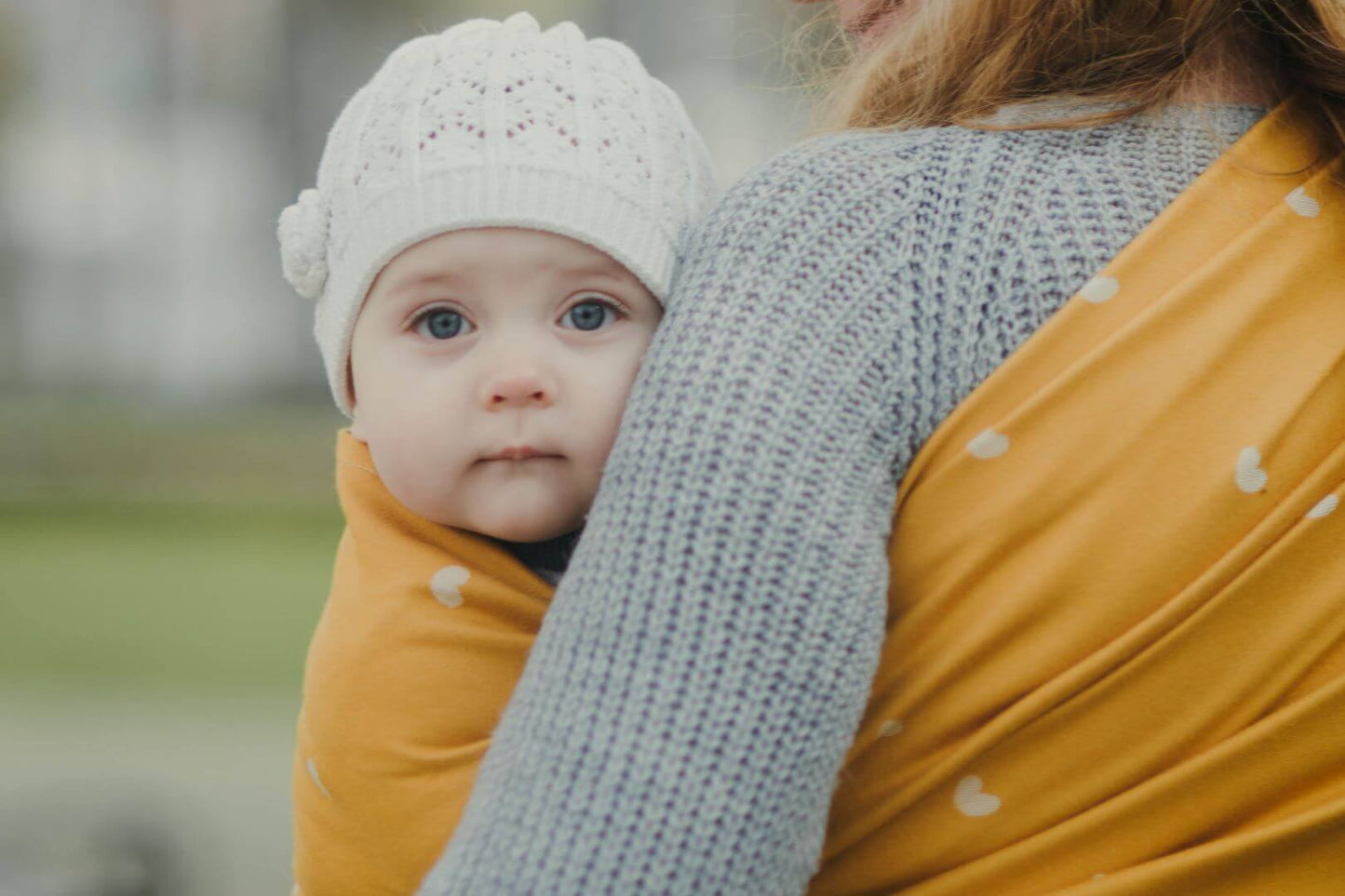 Baby in a ring sling baby carrier in mustard yellow.