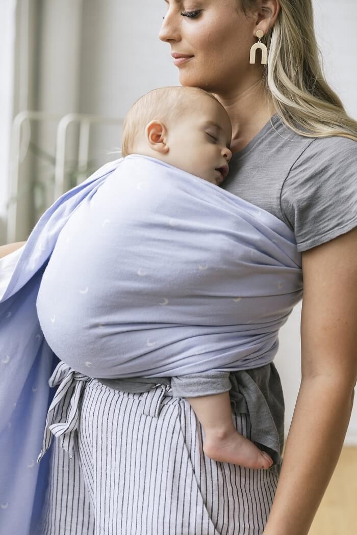 Mum wearing baby in a tula Signature woven baby ring sling with moons twilight pattern in powder blue.