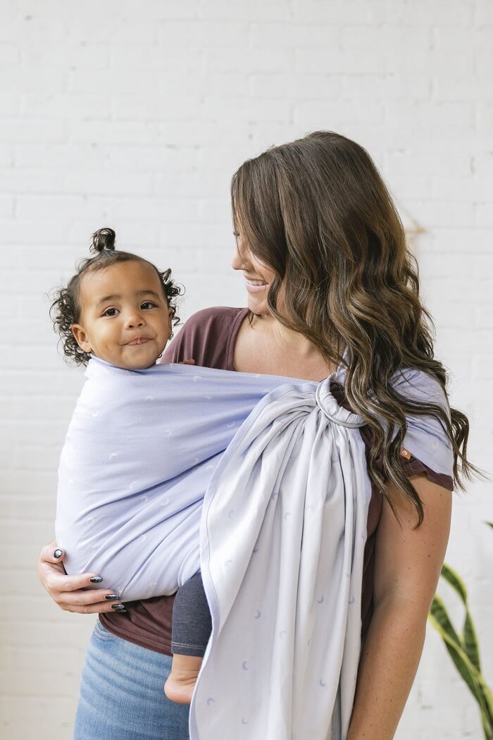 Mum wearing toddler in a Tula Signature ring sling carrier from woven fabric in powder blue with white moons.