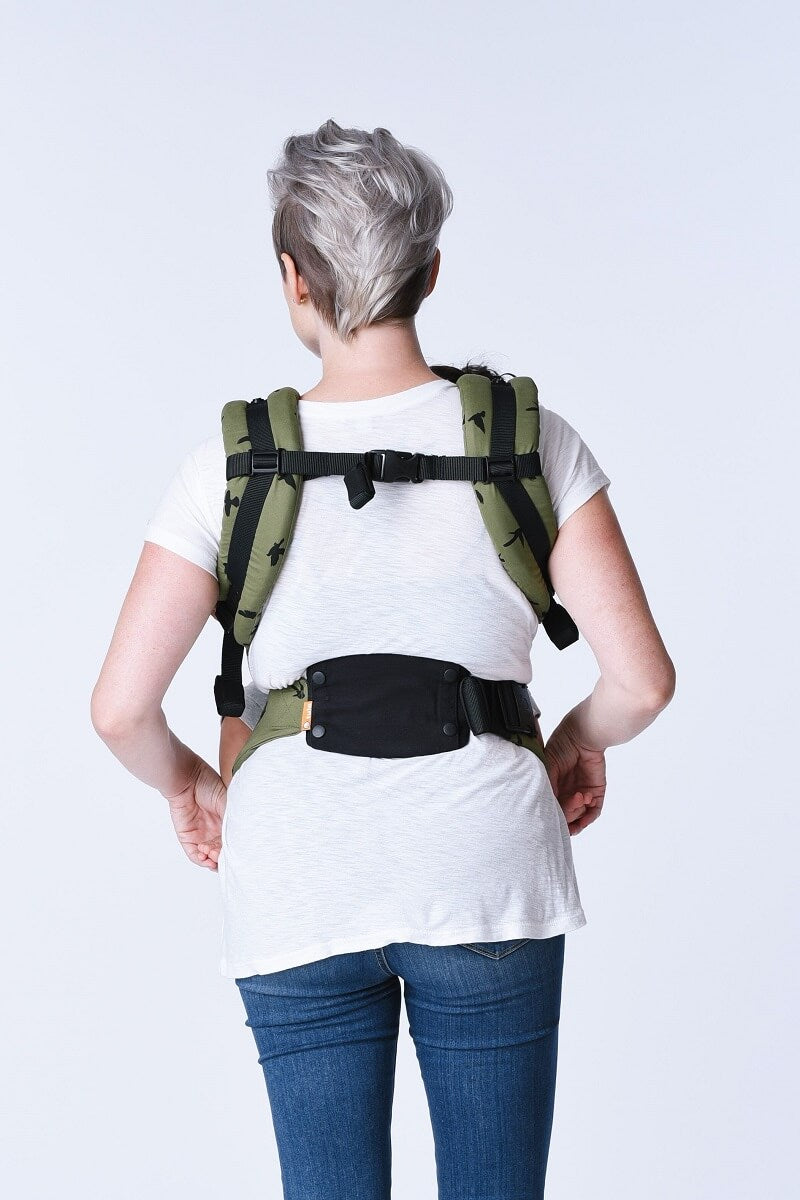 A mother visible from the back, using a baby carrier back support.
