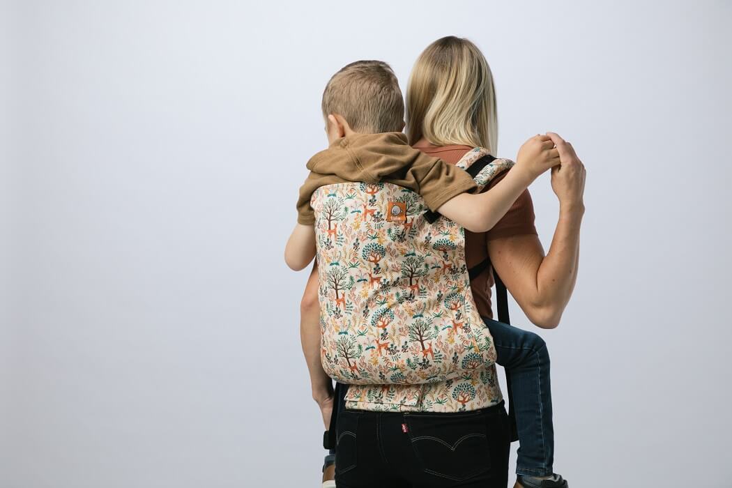 Mum wearing a preschooler in a back carry in an ergomic preschool carrier Charmed by Baby Tula.