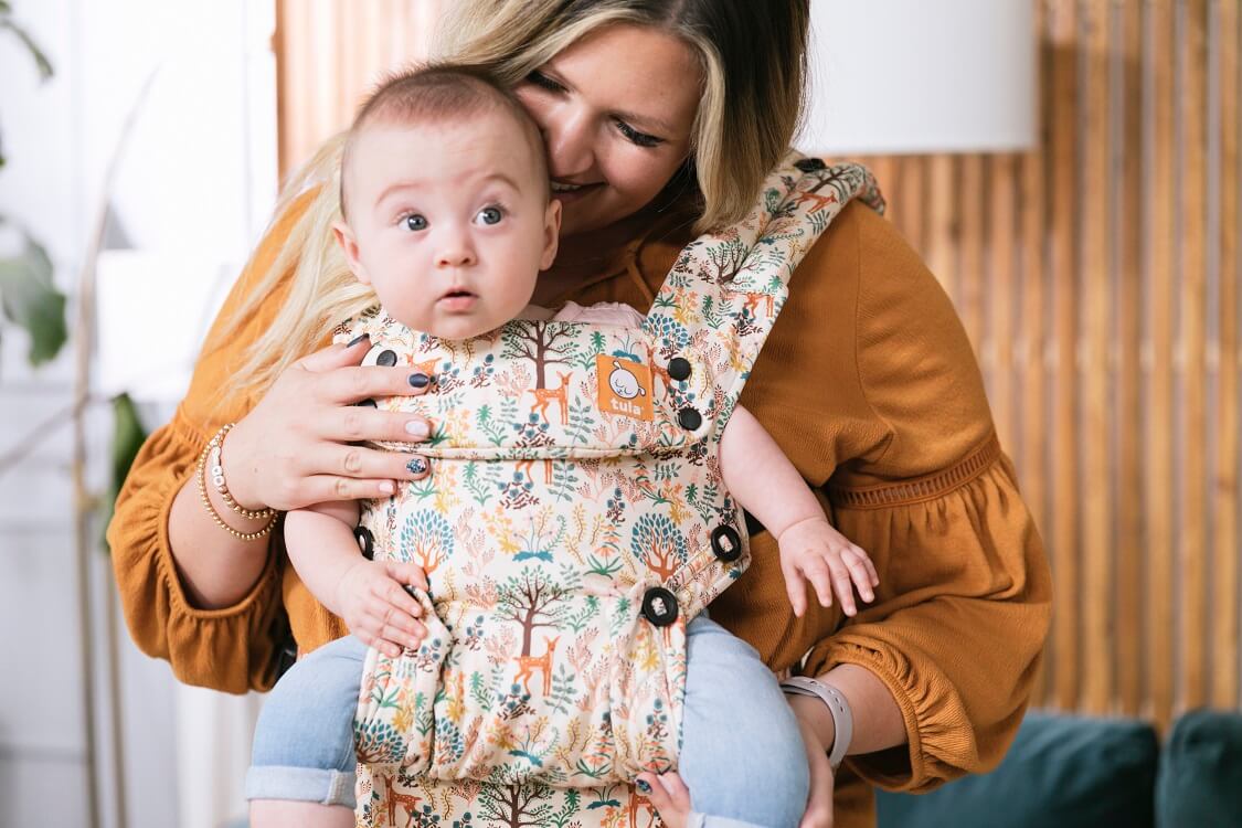 caregiver with an infant in an ergonomic forward facing baby carrier