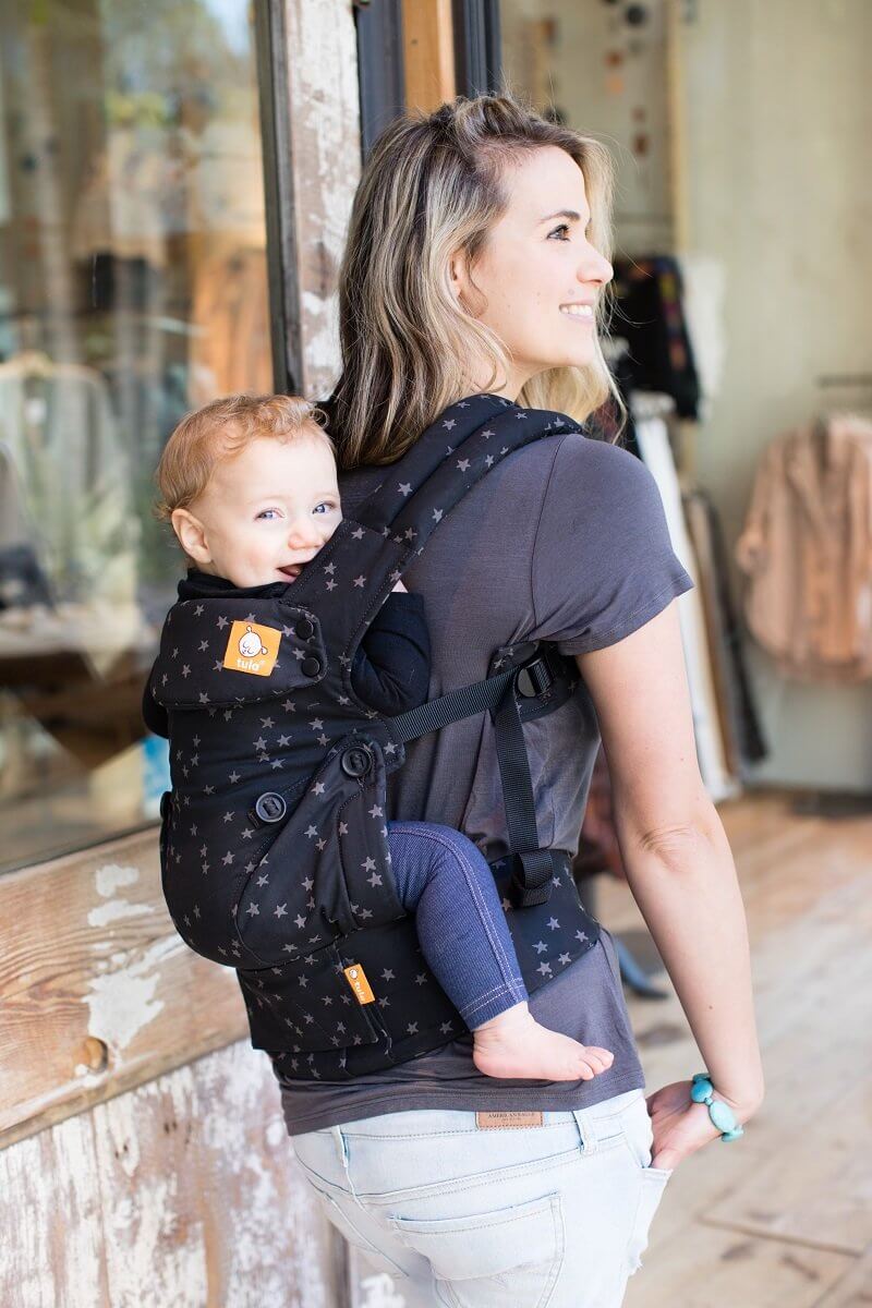 Happy baby worn in a back carry in an ergonomic baby carrier.
