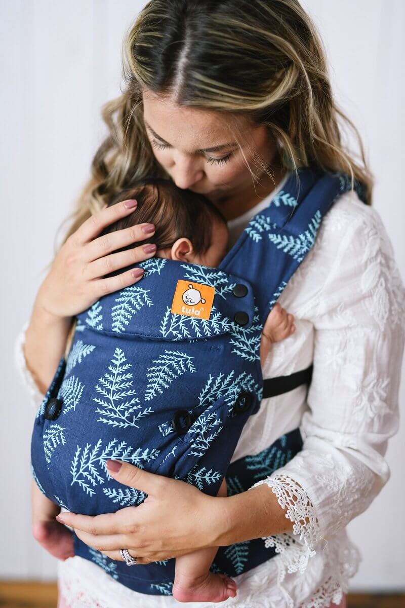 Caregiver embraces small infant in ergonomic baby carrier convenient from birth.