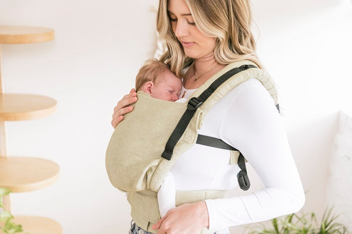 A mother carrying her baby in an ergonomic Free-to-Grow Baby Carrier Linen Moss from Tula.