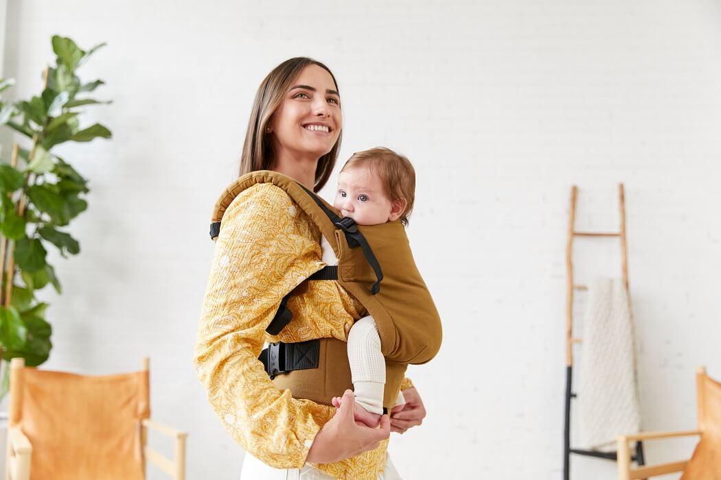 A mother carrying an infant in the ergonomic Free-to-Grow Baby Carrier Olivine in the front-carry position.