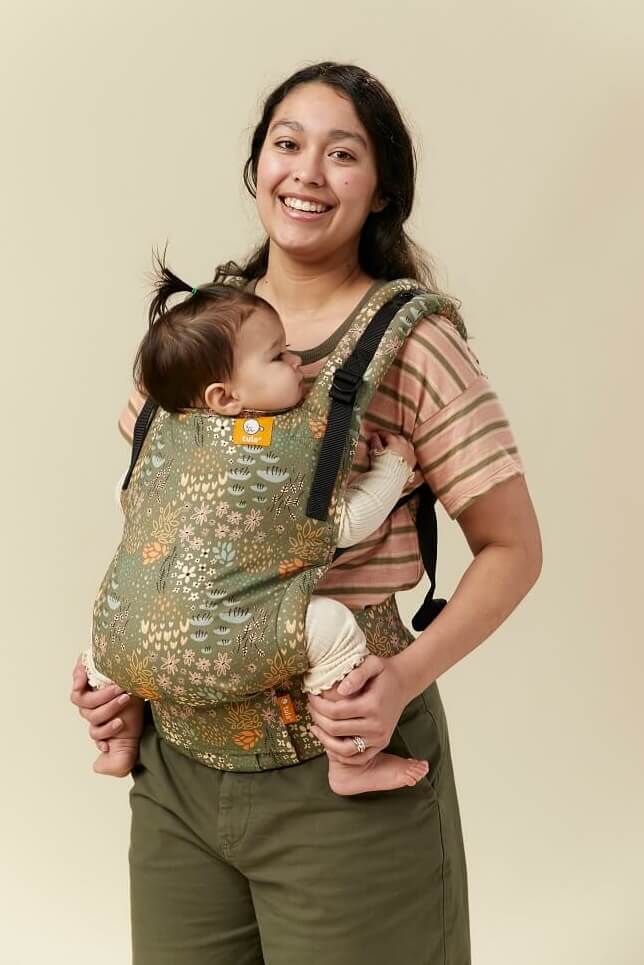 Smiling mother wearing her infant in inward facing position in Tula Free-to-Grow Baby Carrier Meadow