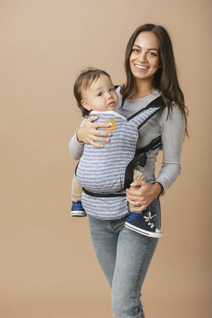 Caregiver wearing baby in a foldable baby carrier in steel blue.