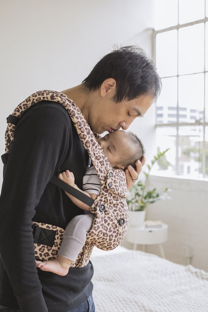 A father giving his baby a kissing. The baby is sitting in the ergonomic Explore Baby Carrier Leopard.