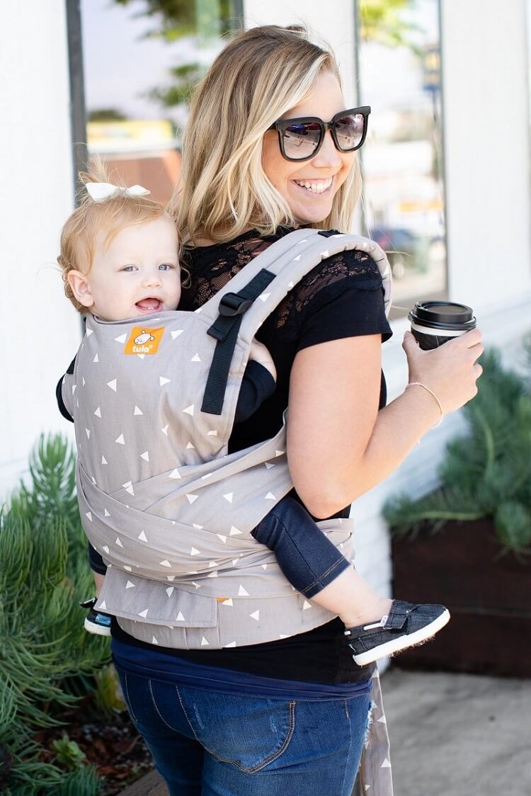 A mother carrying her daughter in the Half Buckle Carrier Sleepy Dust in back-carry position.