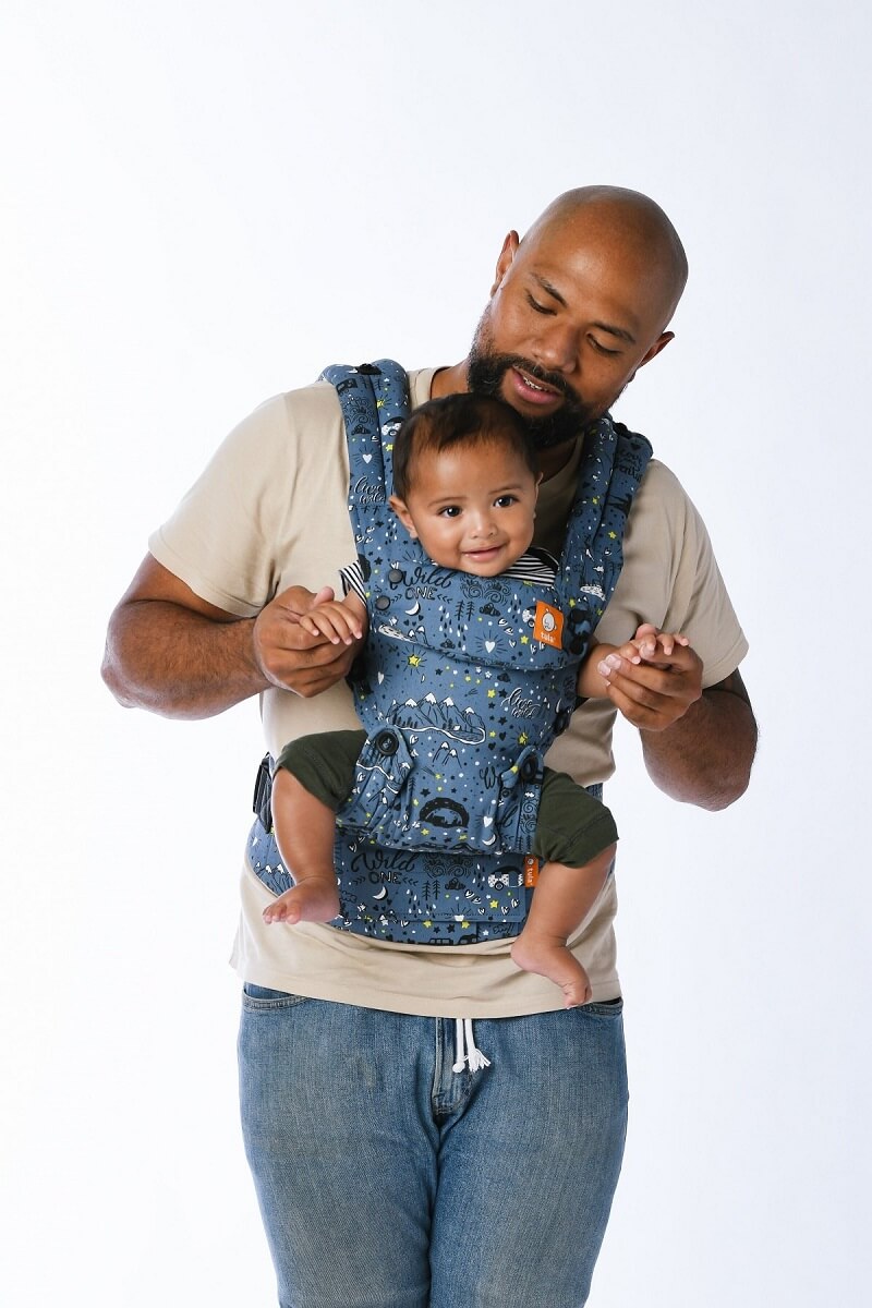 A father looking at his child who is smiling while sitting in the Tula Explore Baby Carrier Wander in forward-facing position.
